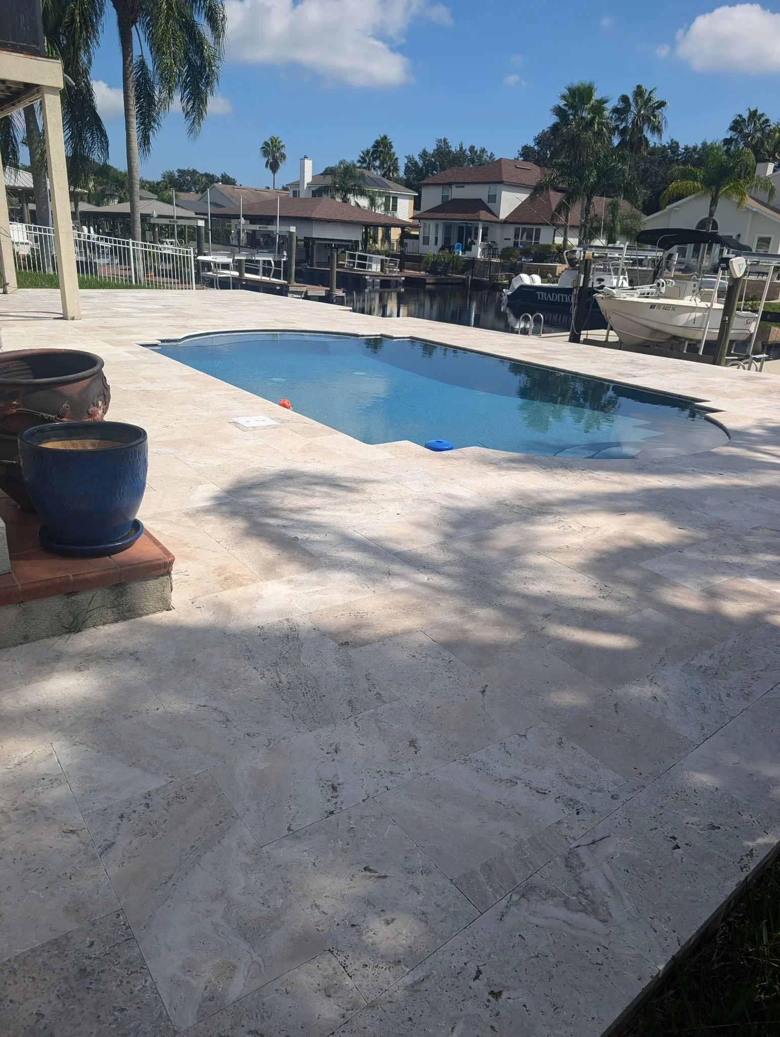 Travertine pool deck with in-ground pool, white railing, and waterfront dock access