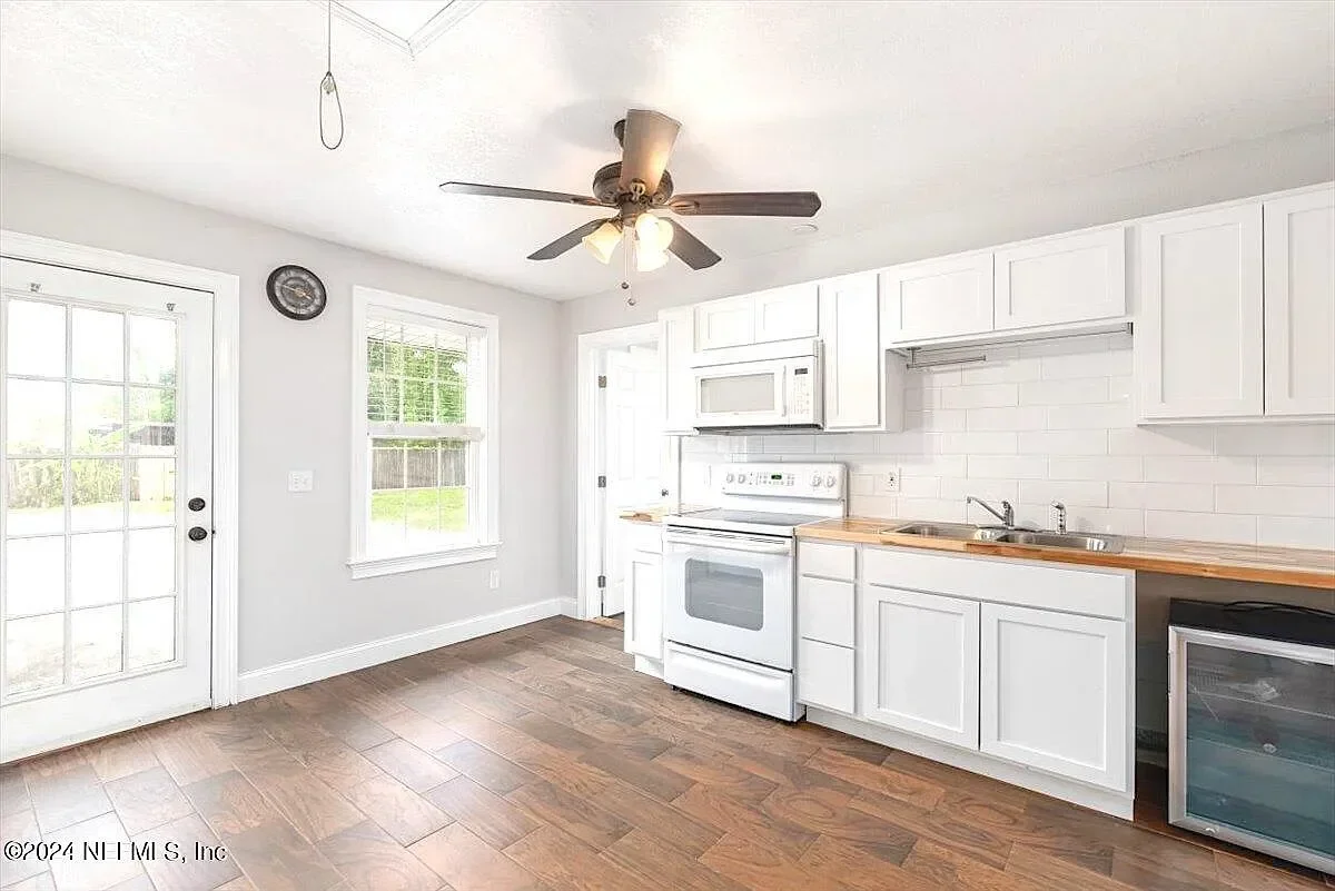 White kitchen cabinets, wood countertops, subway tile backsplash, white appliances, wood-look flooring