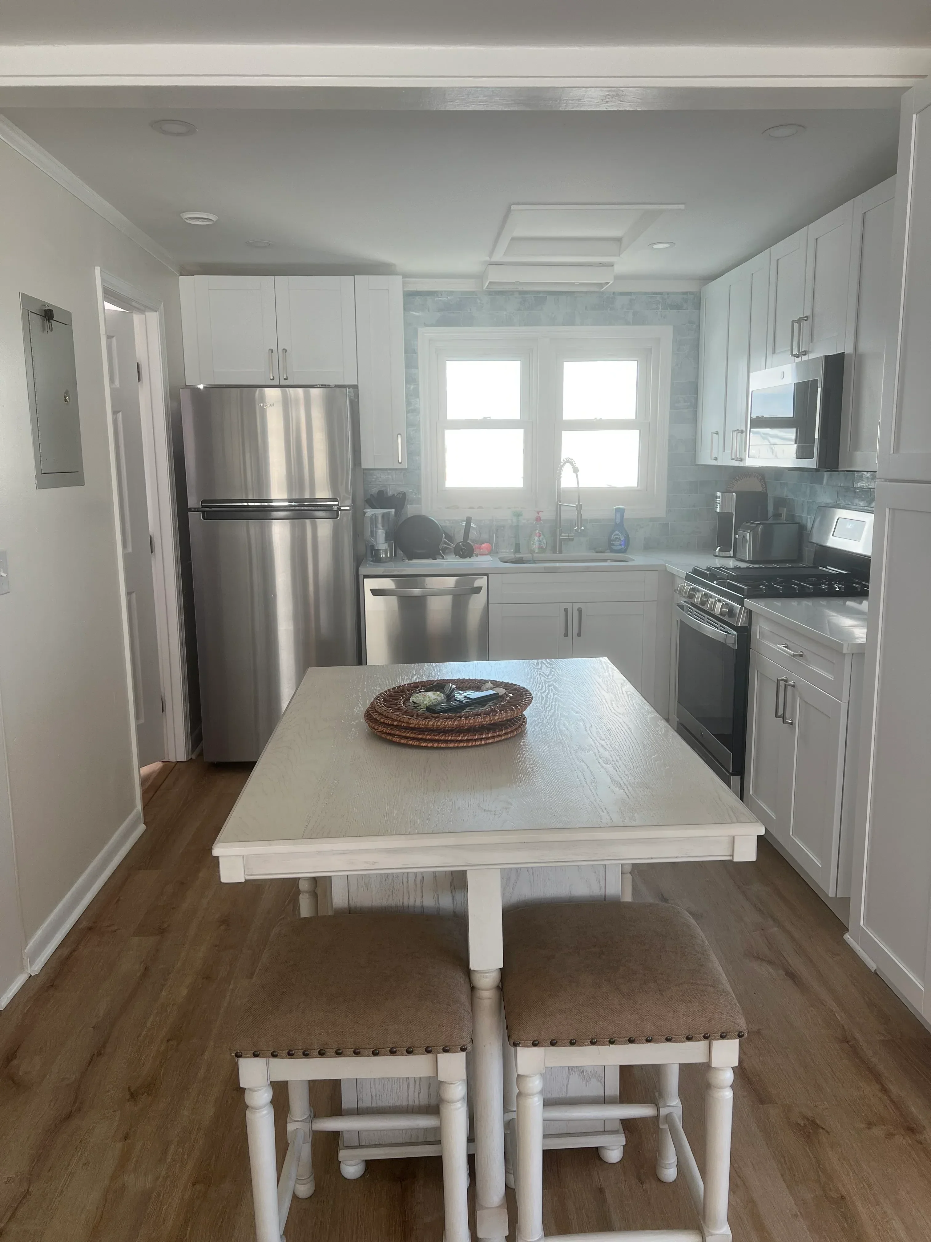 Modern kitchen with white cabinetry, stainless steel appliances, blue tile backsplash, and bathroom with heated towel rack