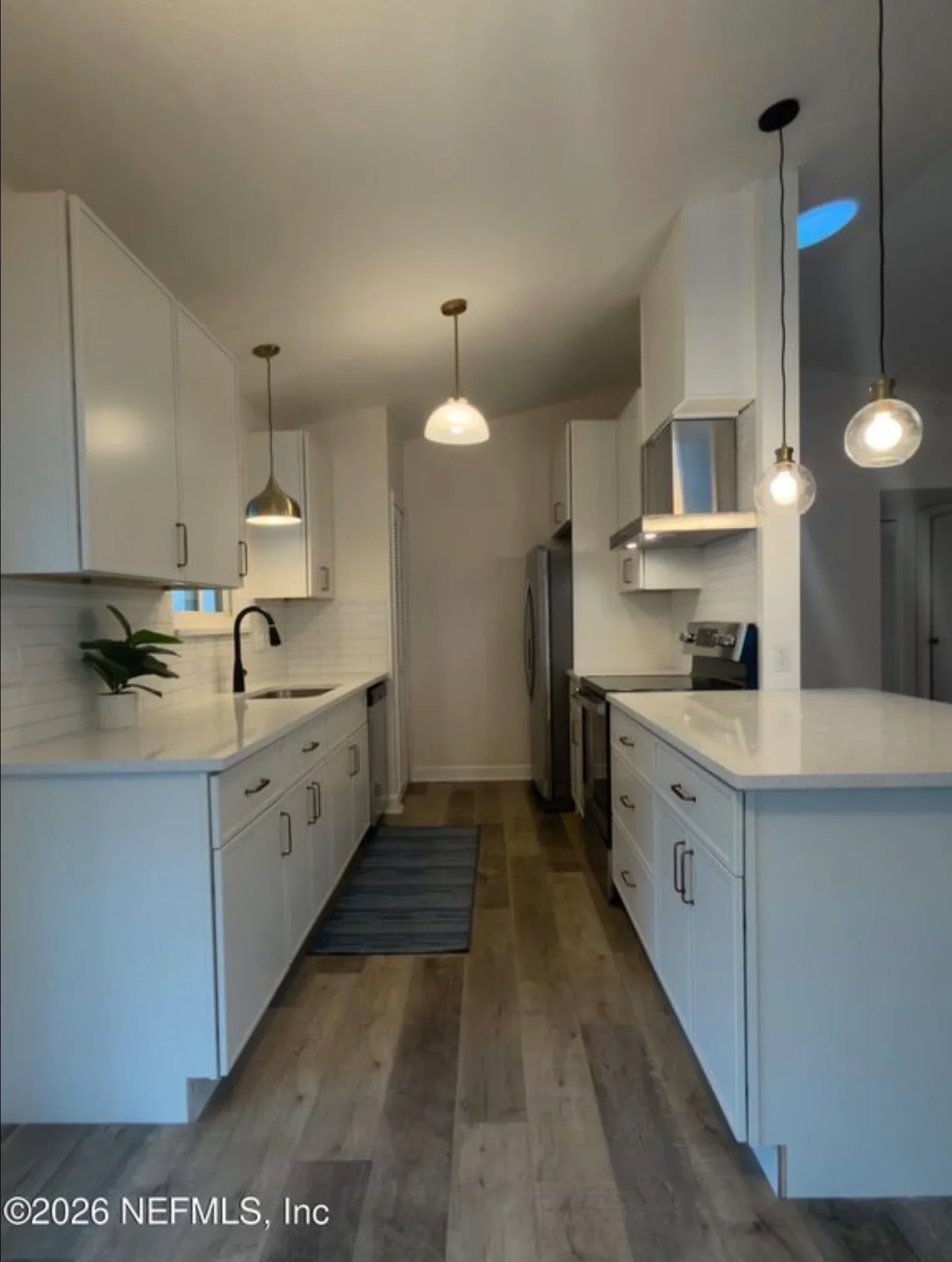 White kitchen with subway tile backsplash, quartz counters, pendant lights, and hardwood flooring
