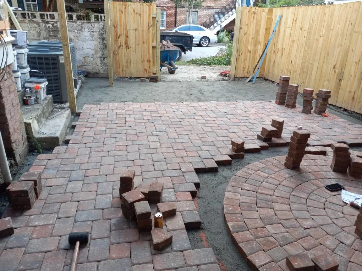 Clay brick paver patio installation with running bond pattern and wooden fence enclosure