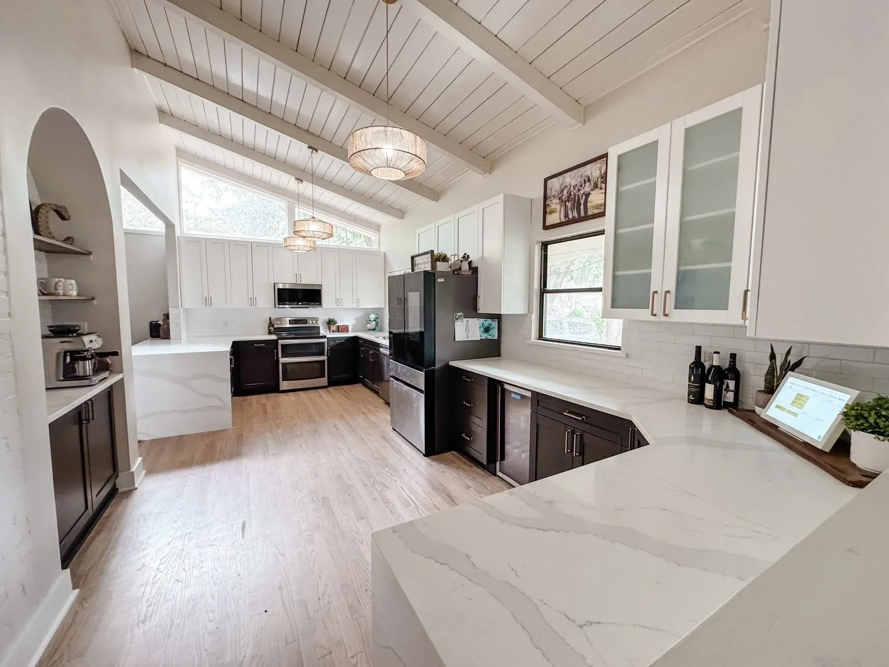 Modern kitchen with white and dark cabinetry, quartz counters, stainless appliances, and vaulted ceilings
