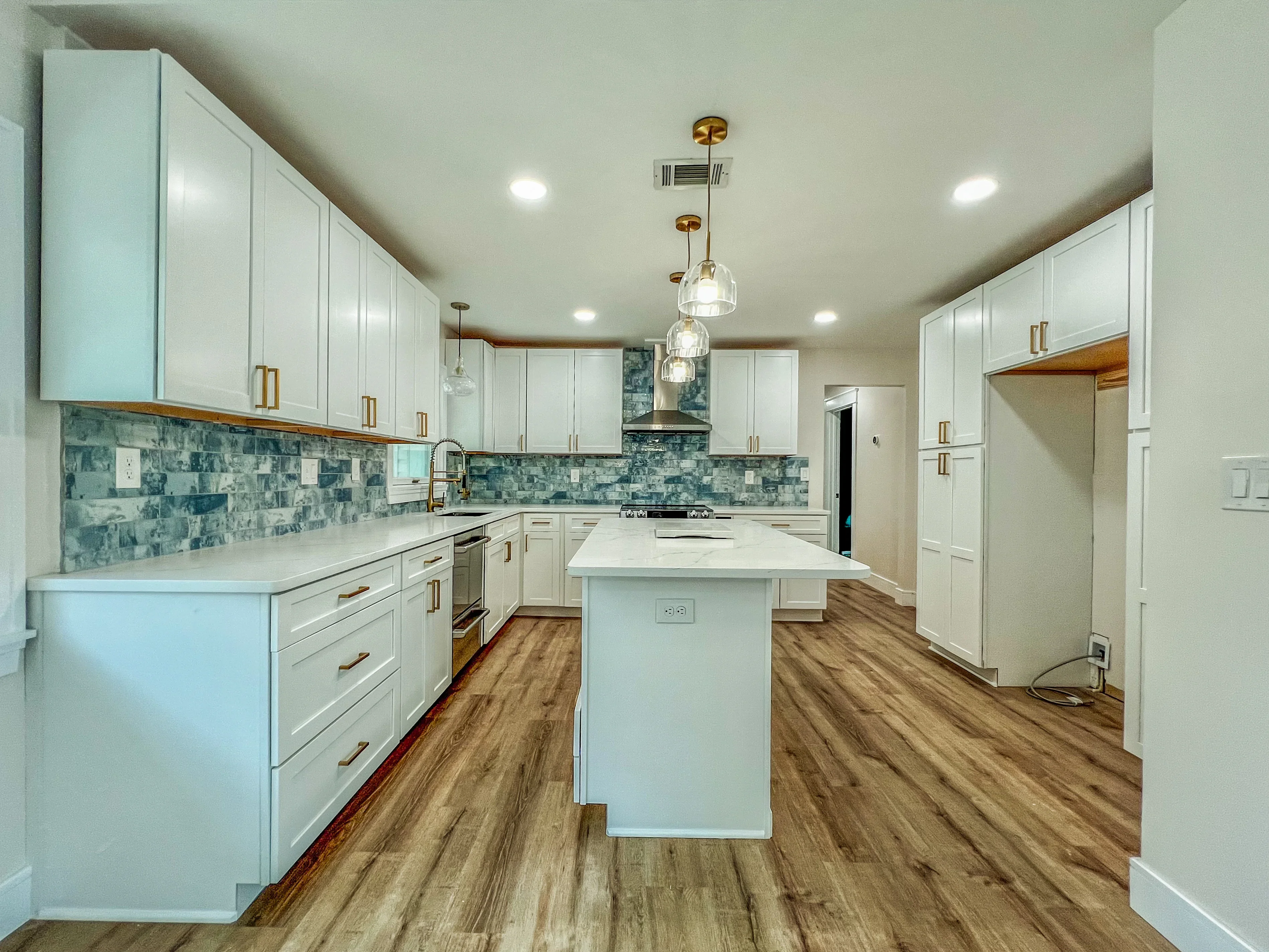 White kitchen cabinets, blue tile backsplash, white island, brass fixtures, wood flooring