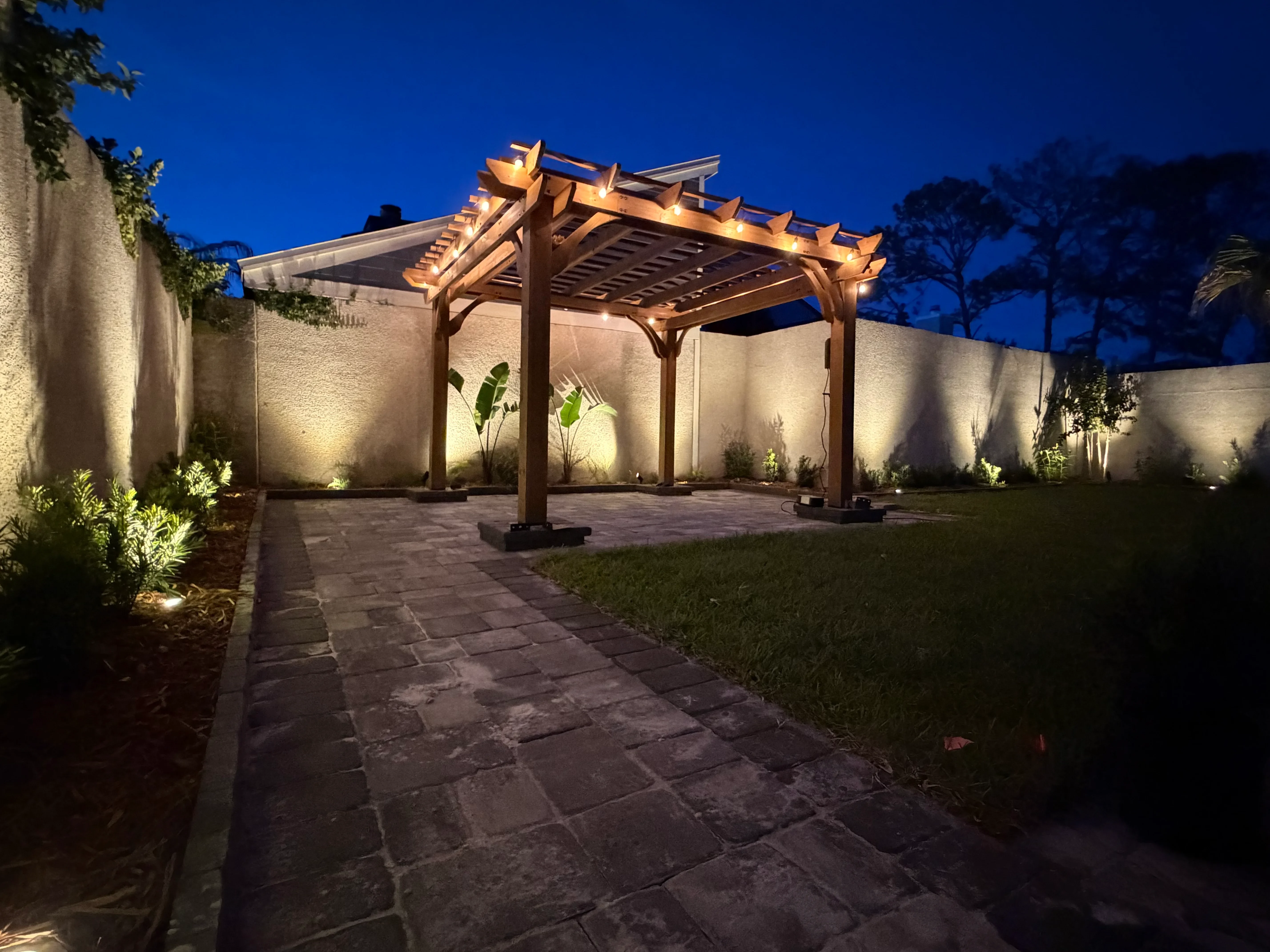 Illuminated wooden pergola with uplighting on stone patio and accent-lit perimeter walls