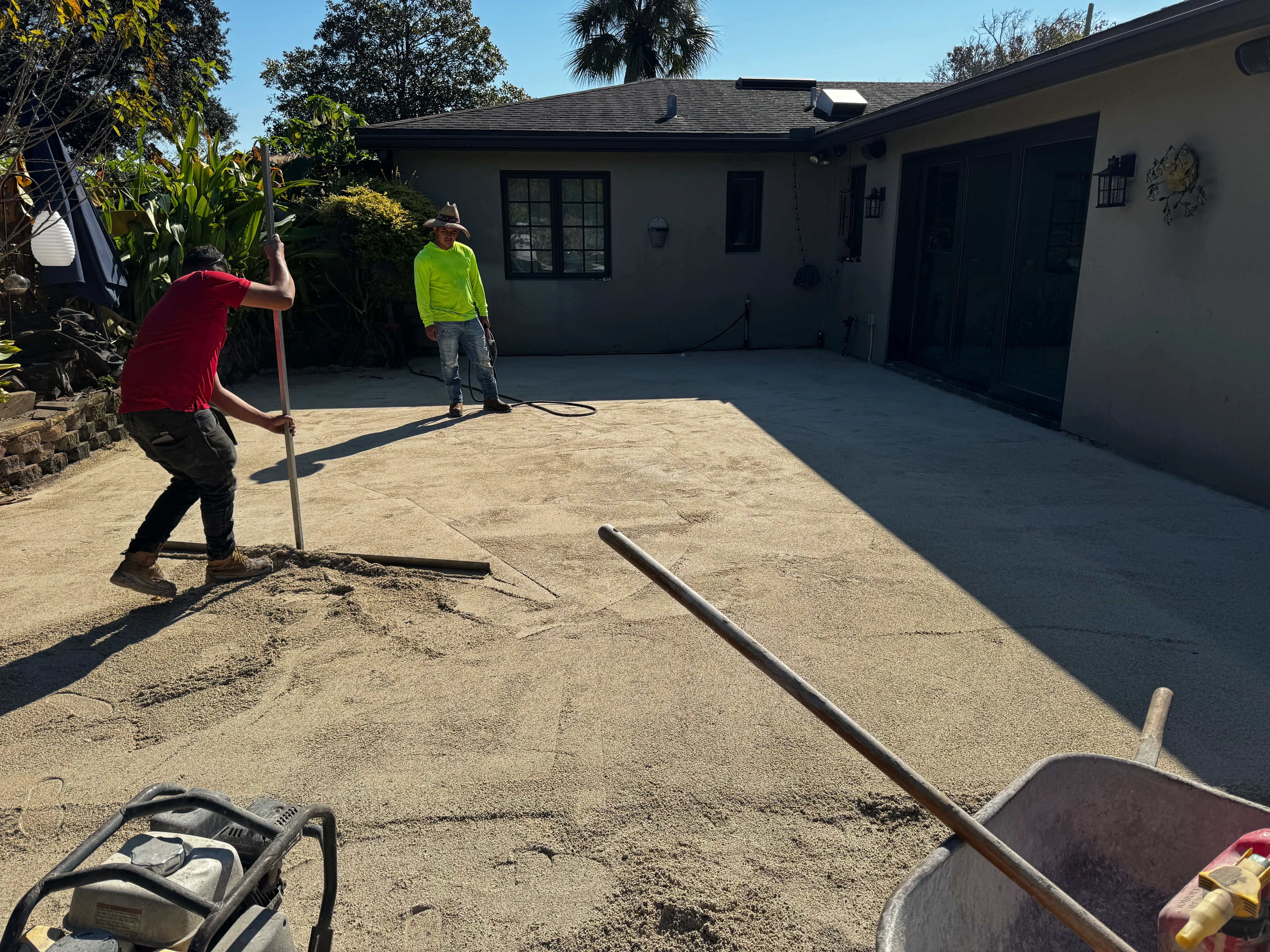 Driveway base preparation with workers grading compacted soil and aggregate material