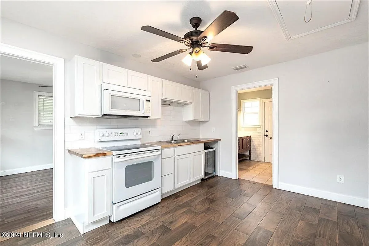 White kitchen cabinets, wood-look tile floor, white appliances, and ceiling fan with lighting