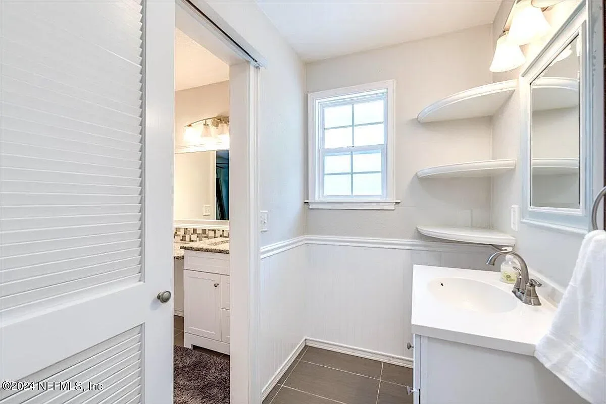 Renovated bathroom with white vanity, floating shelves, beadboard wainscoting, and ceramic tile flooring