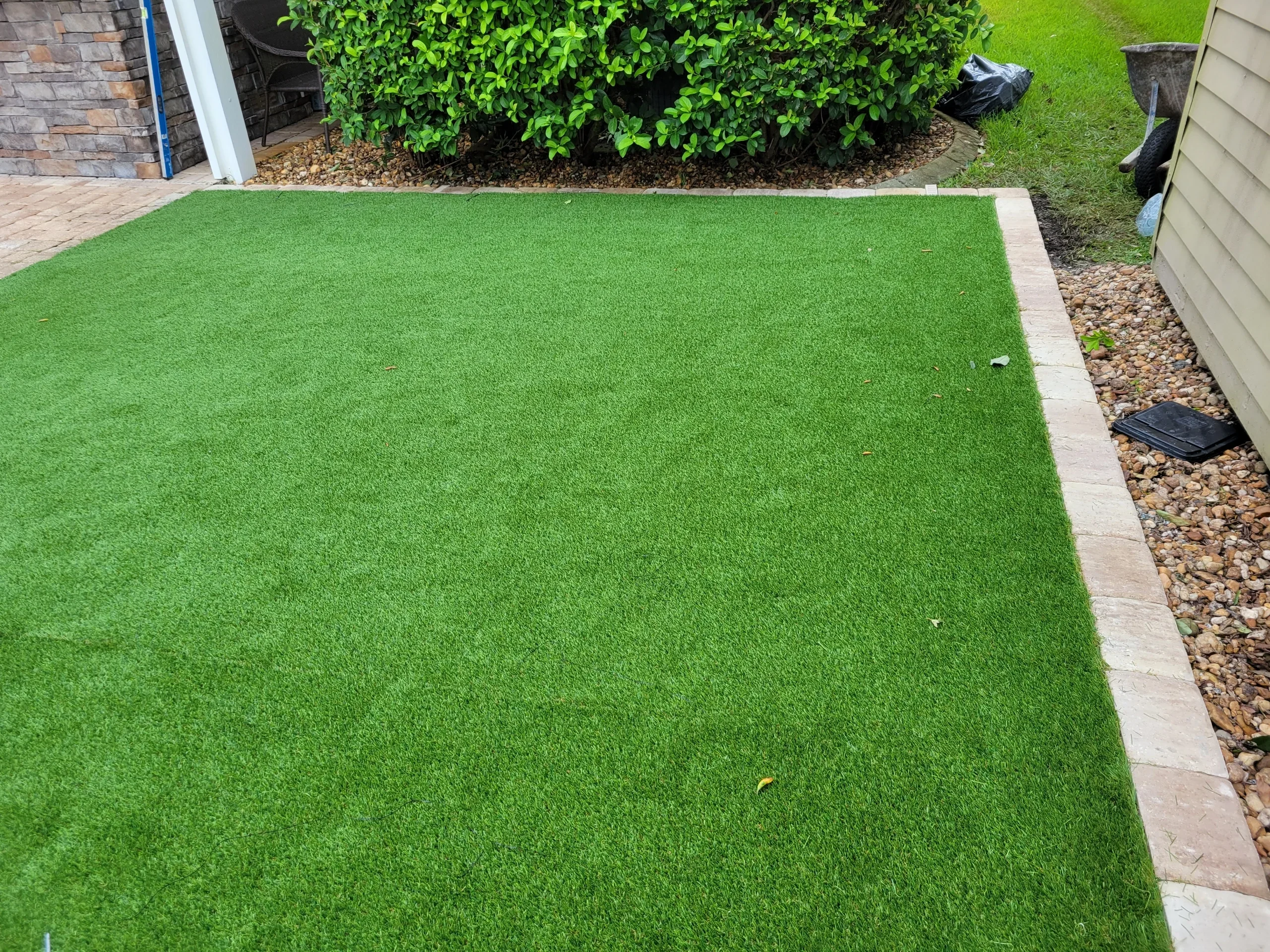 Artificial turf lawn with concrete border edging and river rock landscaping