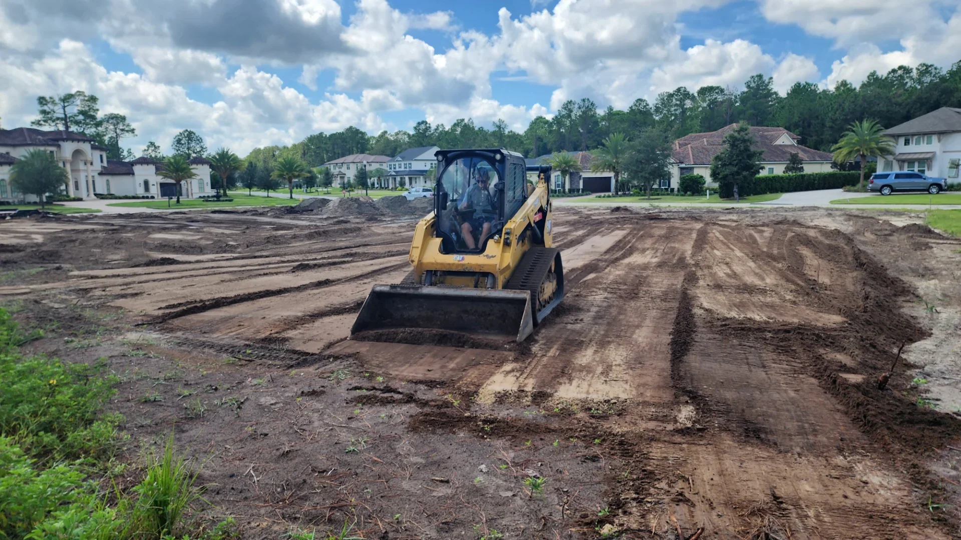 Yellow skid steer loader grading and compacting soil on residential construction site