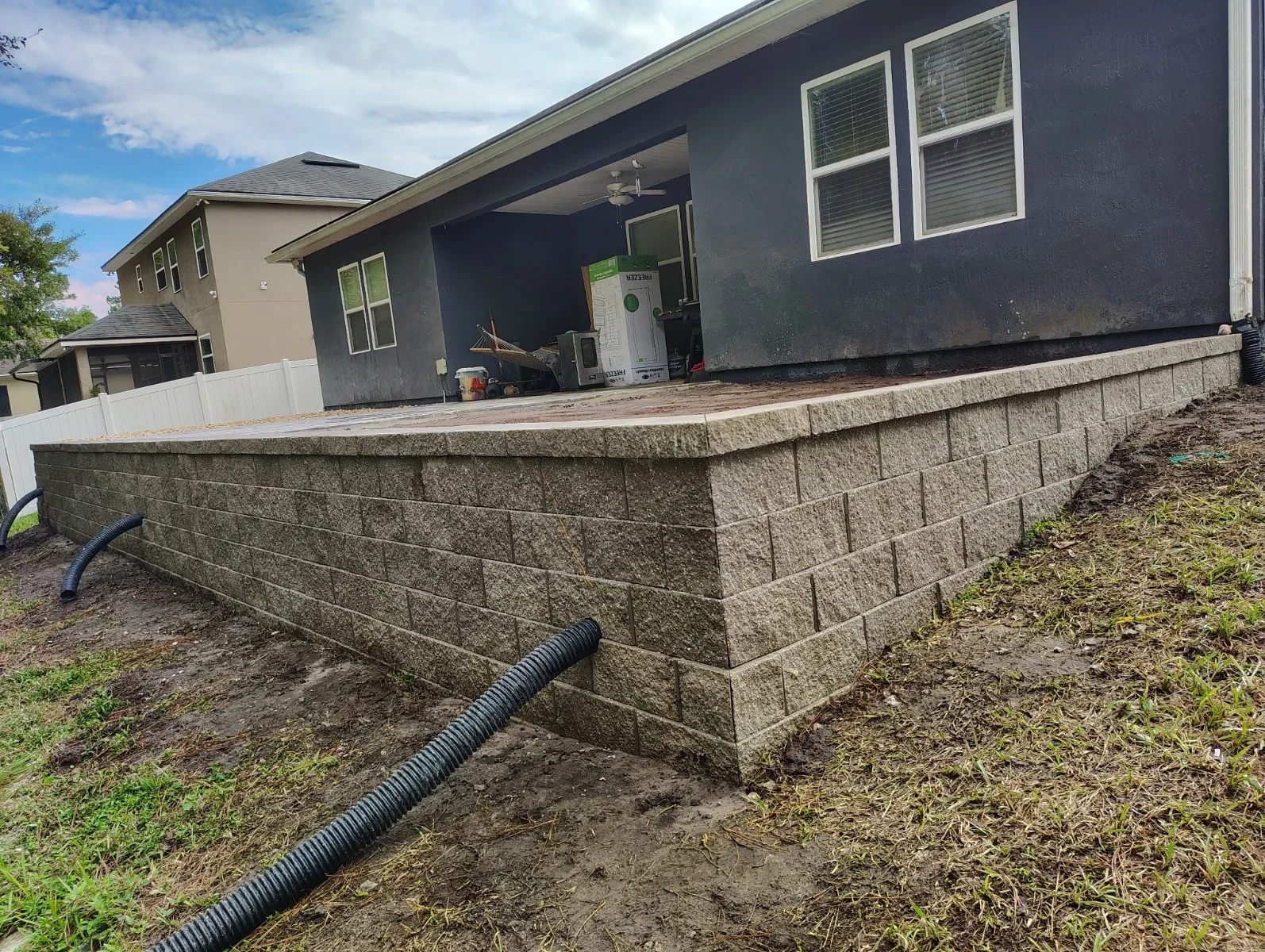 Concrete block retaining wall with drainage pipe and cap blocks installed along residential property