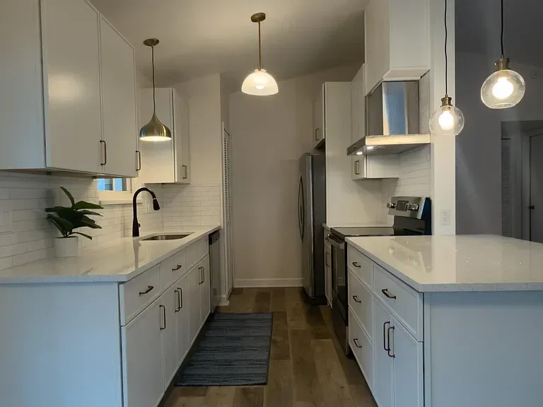 White kitchen with subway tile, quartz counters, pendant lights, and stainless steel appliances