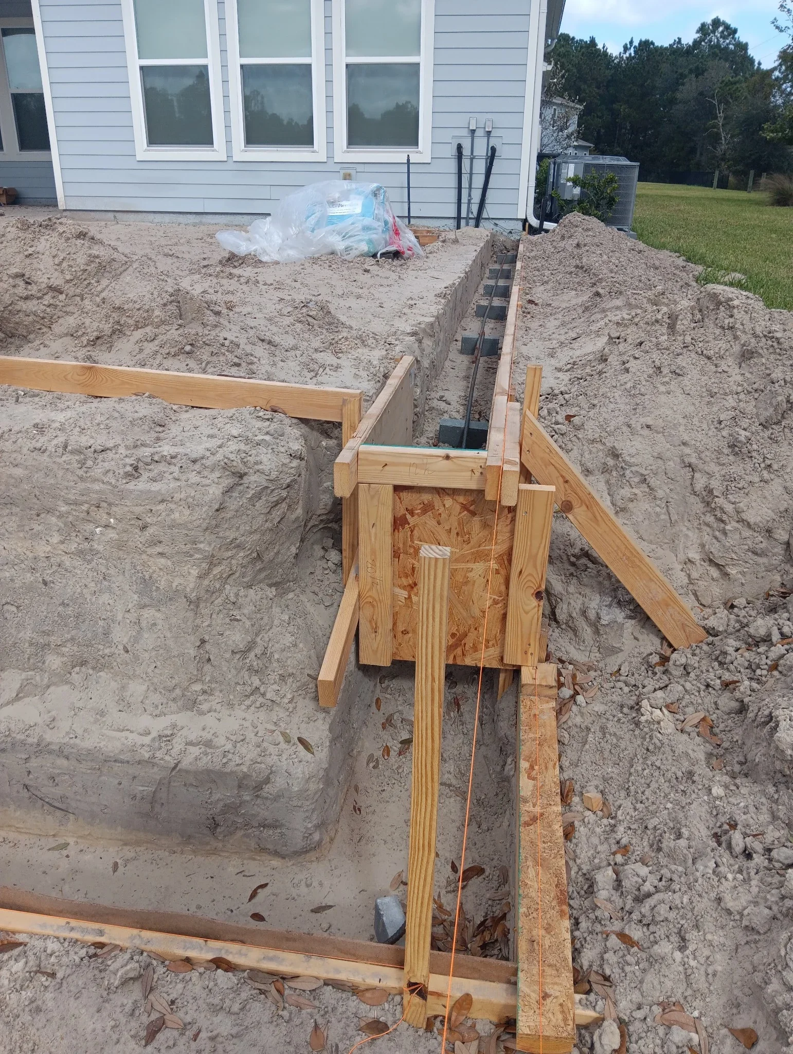 Wooden-shored excavation trench with PVC conduit and electrical lines for foundation work