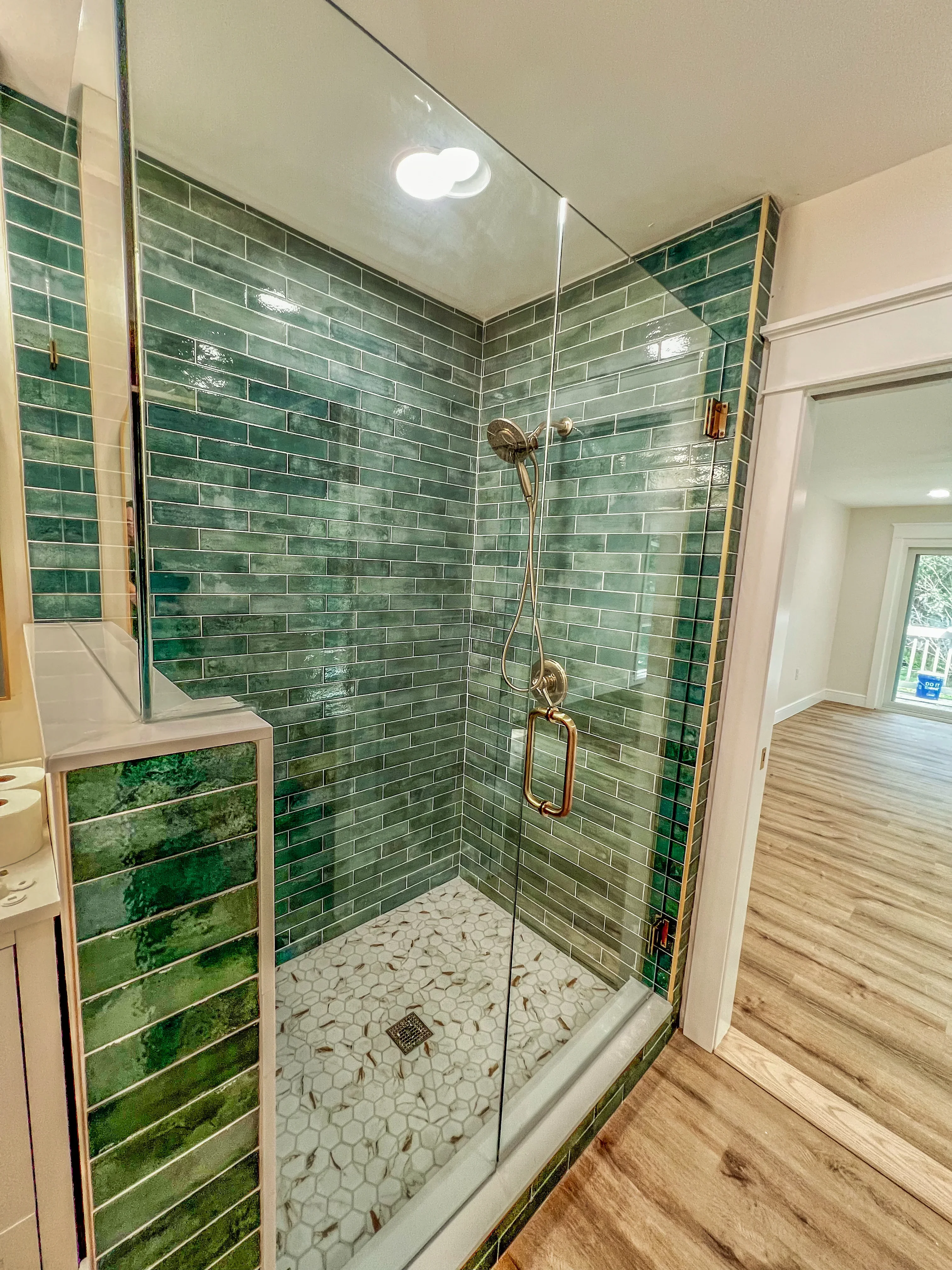 Green subway tile shower with marble hexagon floor, brass fixtures, and frameless glass enclosure