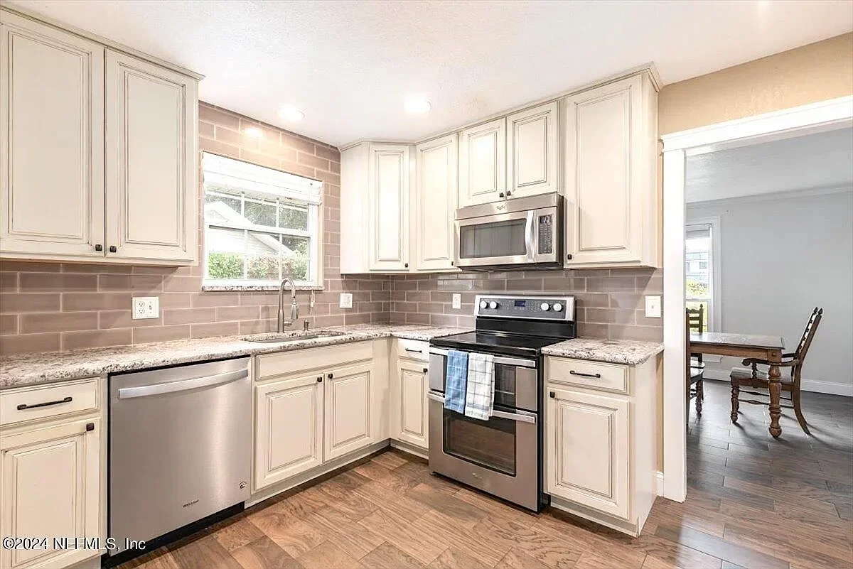Cream cabinetry kitchen with granite counters, subway tile backsplash, and stainless steel appliances