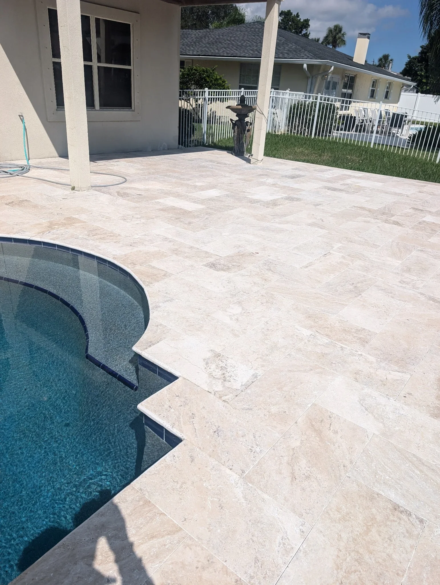 Travertine pool deck with large format pavers installed around curved pool edge