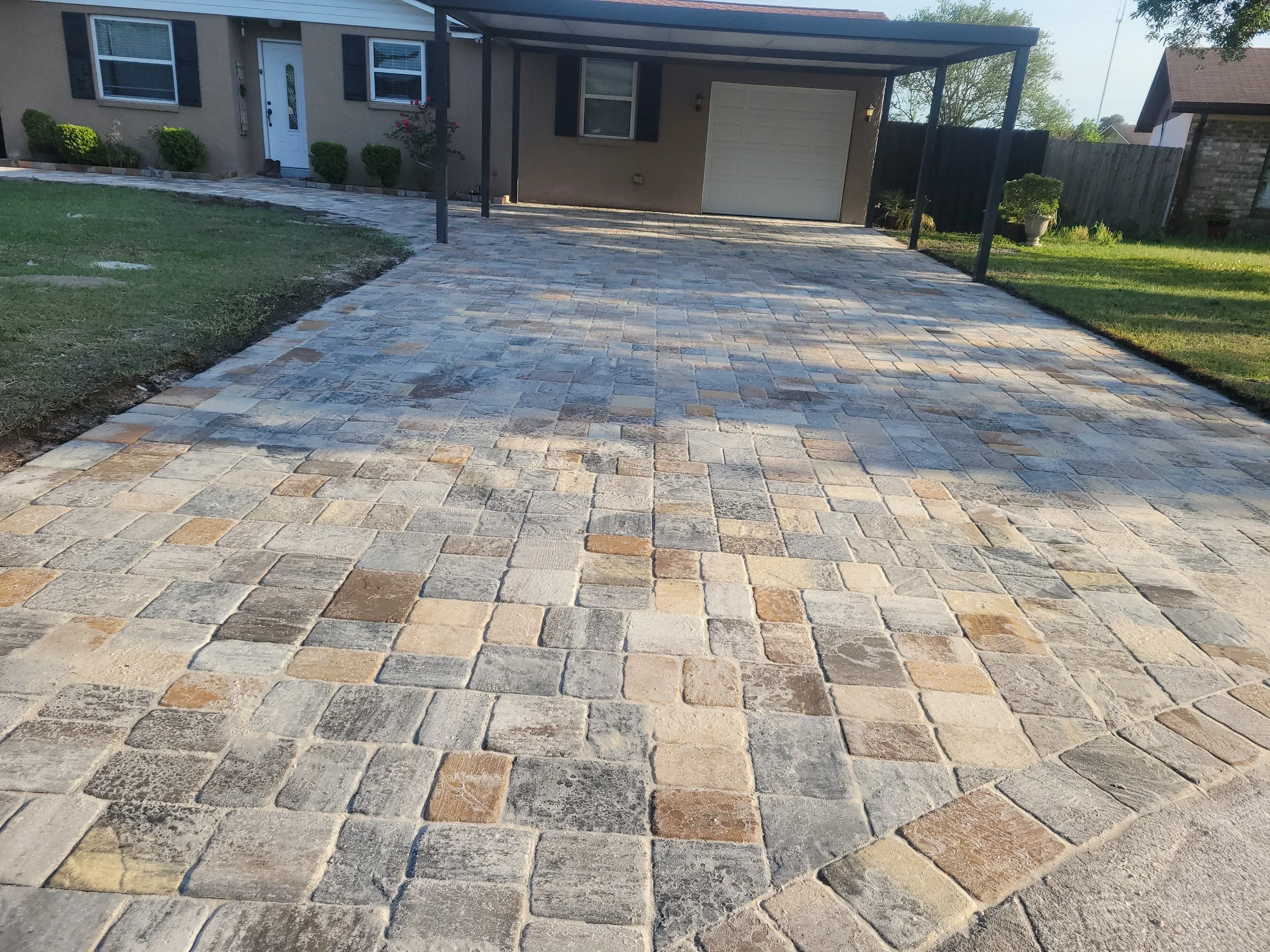 Permeable stone pavers in mixed earth tones installed as residential driveway with pergola overhead