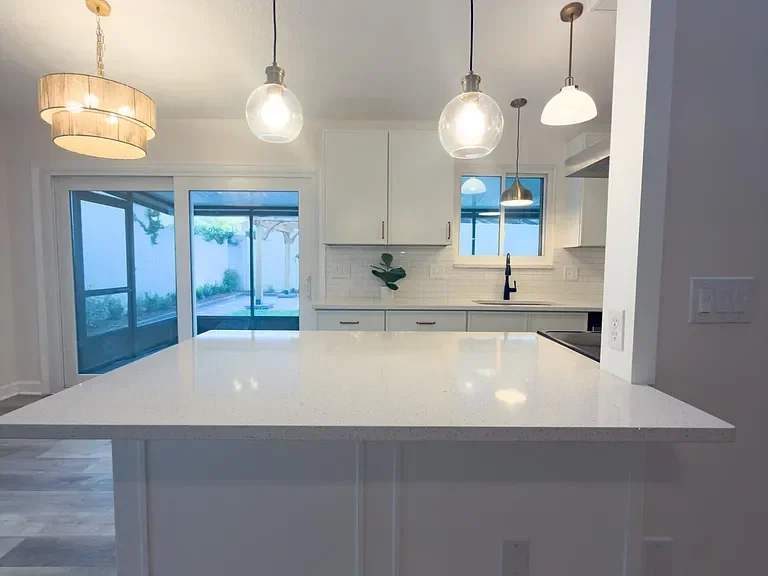 Modern kitchen with white island, quartz countertop, white cabinetry, subway tile backsplash, and pendant lighting